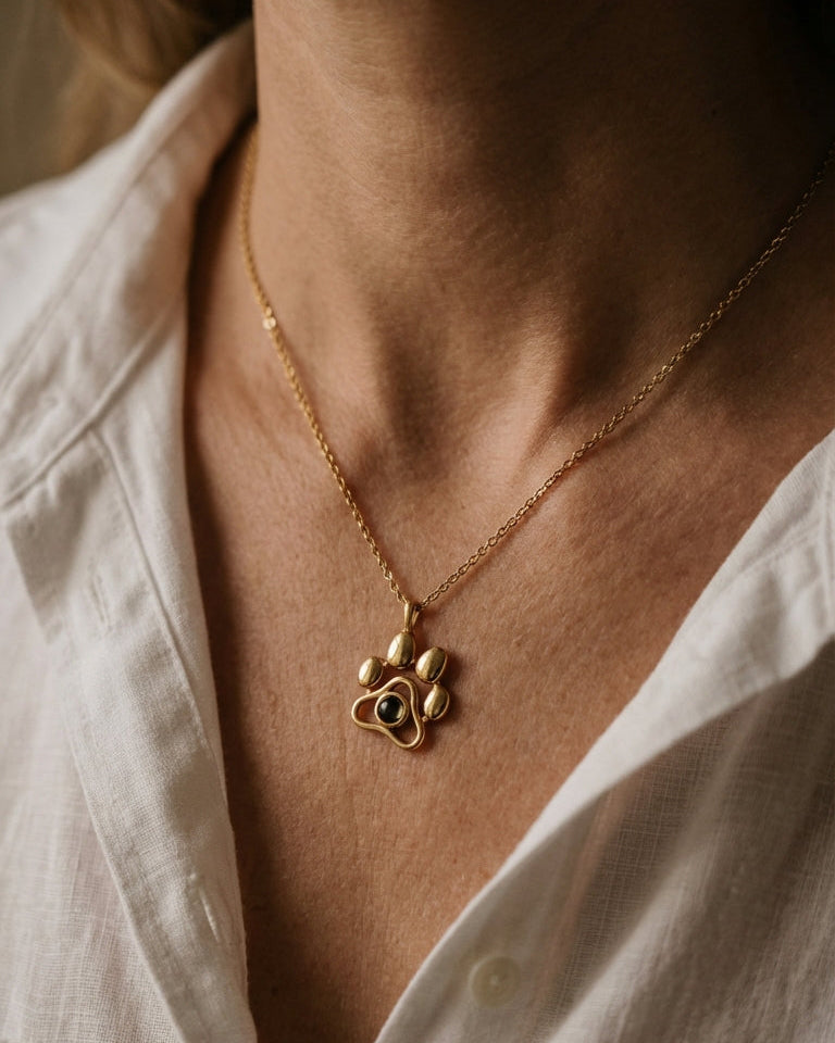 Gold necklace with a paw-shaped pendant worn by a person in a white shirt.