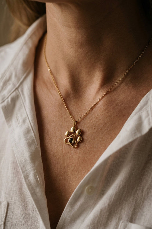 Gold necklace with a paw-shaped pendant worn by a person in a white shirt.