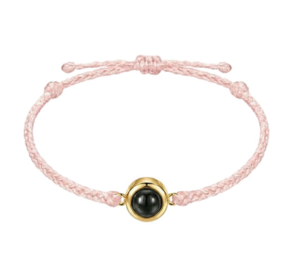 Pink braided bracelet with a black bead and gold accent on a white background